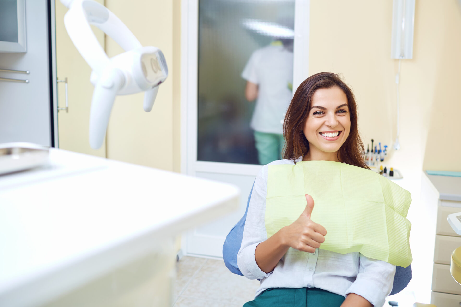 Patient woman smiling holding thumbs up at the dental clinic.